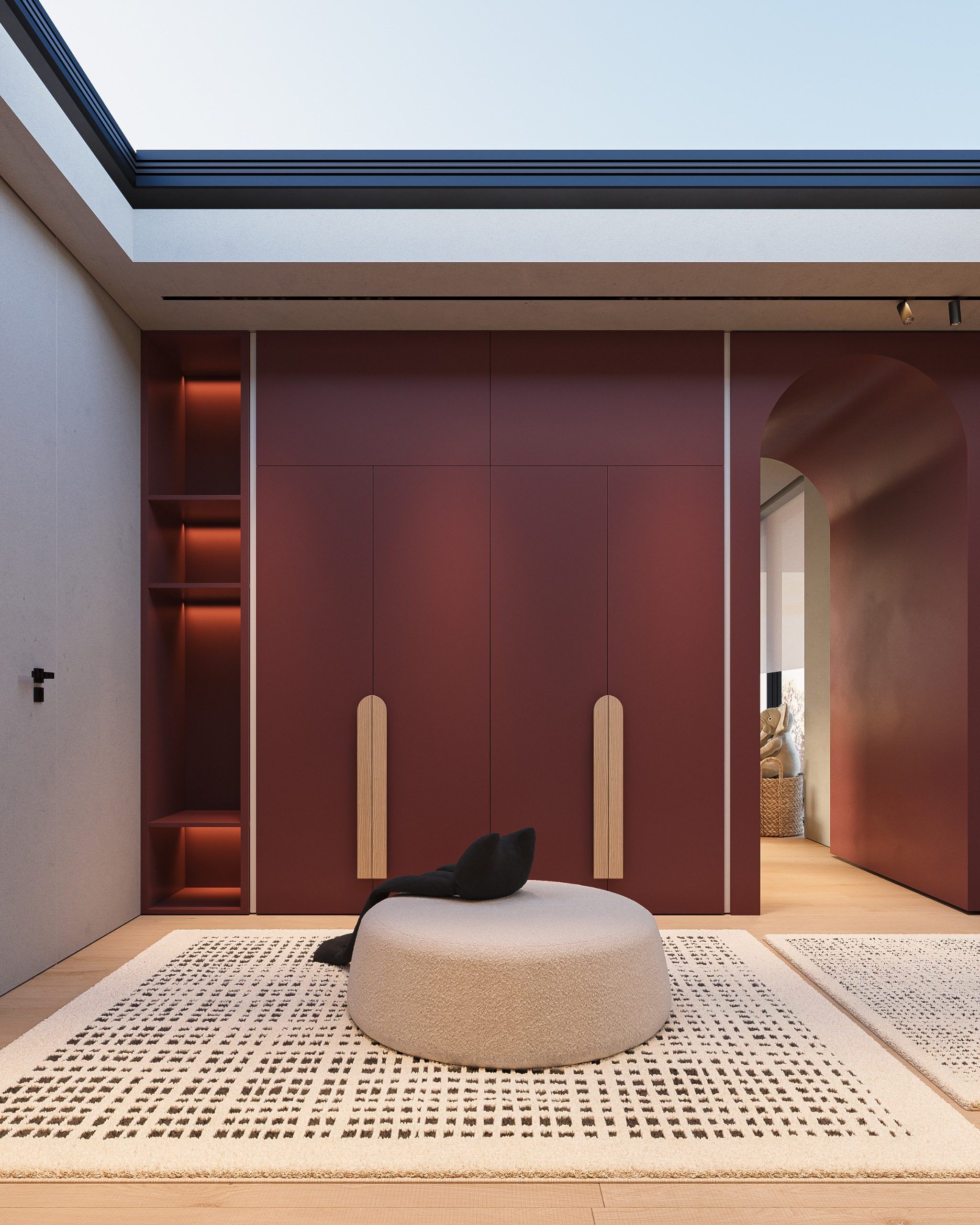 Round bed centered in room with burgundy and light cabinetry on sides, natural light from above